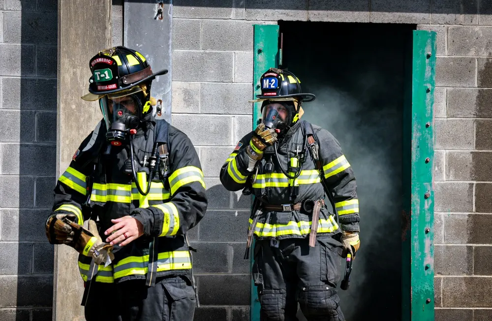 Firefighters wearing breathing apparatus exit a smoke-filled training building